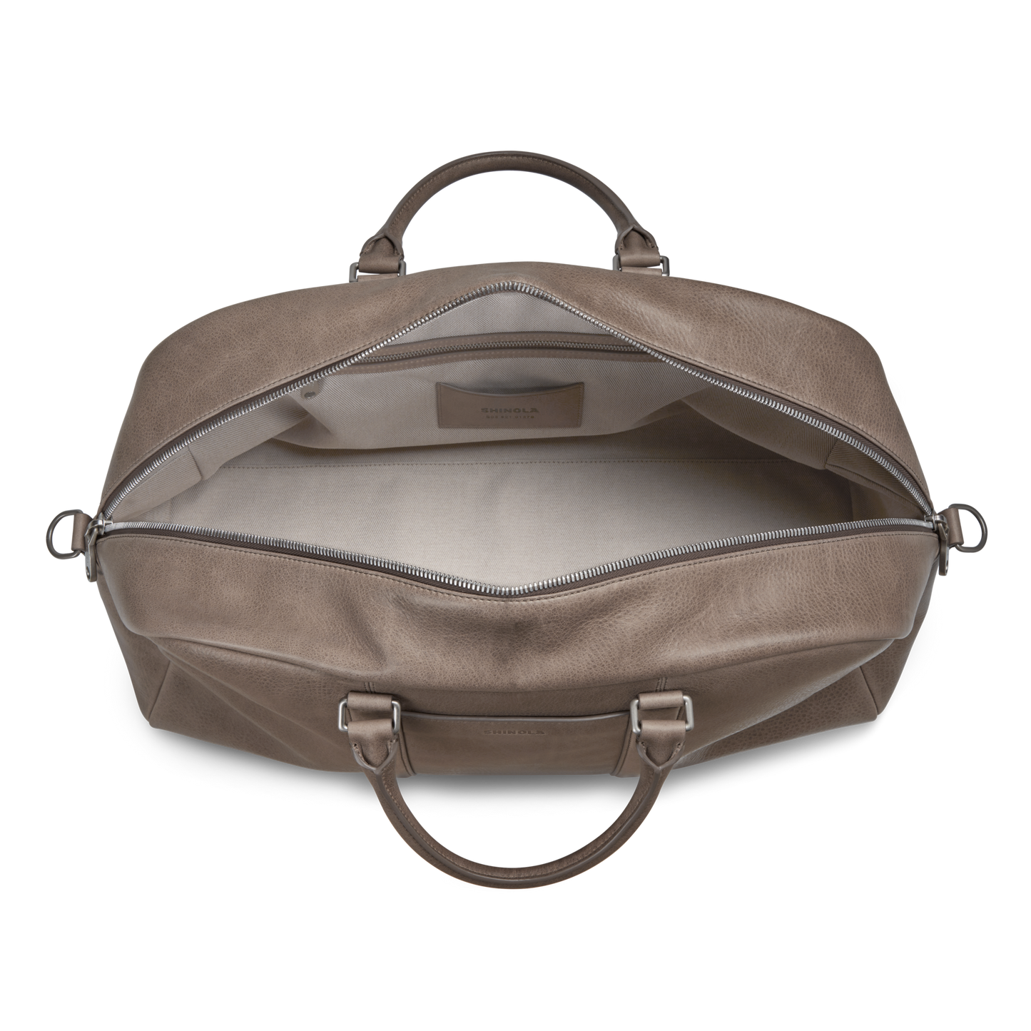 The Shinola Runwell Duffle Bag - Stone is seen open from above, showcasing its roomy light interior, zippered closure, leather handles, and metal hardware in natural grain leather.
