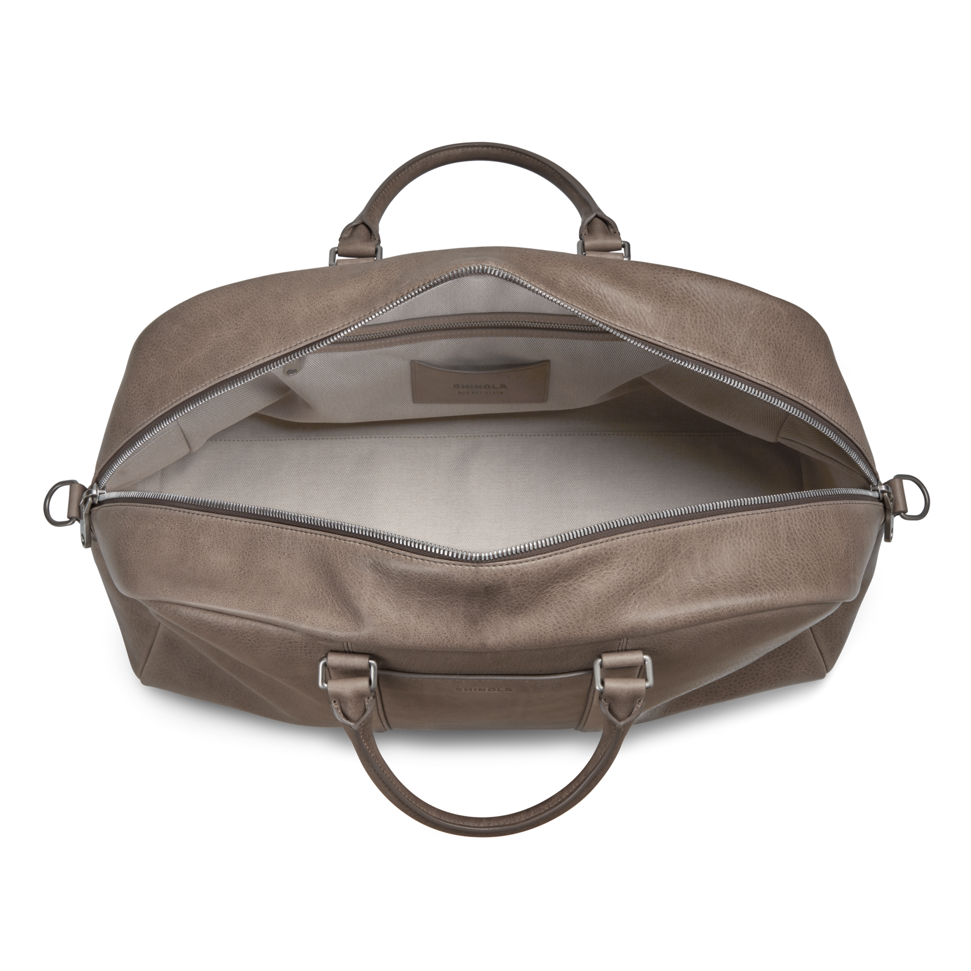 The Shinola Runwell Duffle Bag - Stone is seen open from above, showcasing its roomy light interior, zippered closure, leather handles, and metal hardware in natural grain leather.