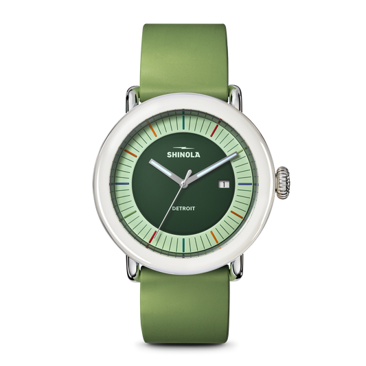 The Shinola Detrola Watch - Deep Olive features a round face, light green dial, white bezel, and green leather strap. This modern wristwatch displays the date and has colorful markers encircling the edge.