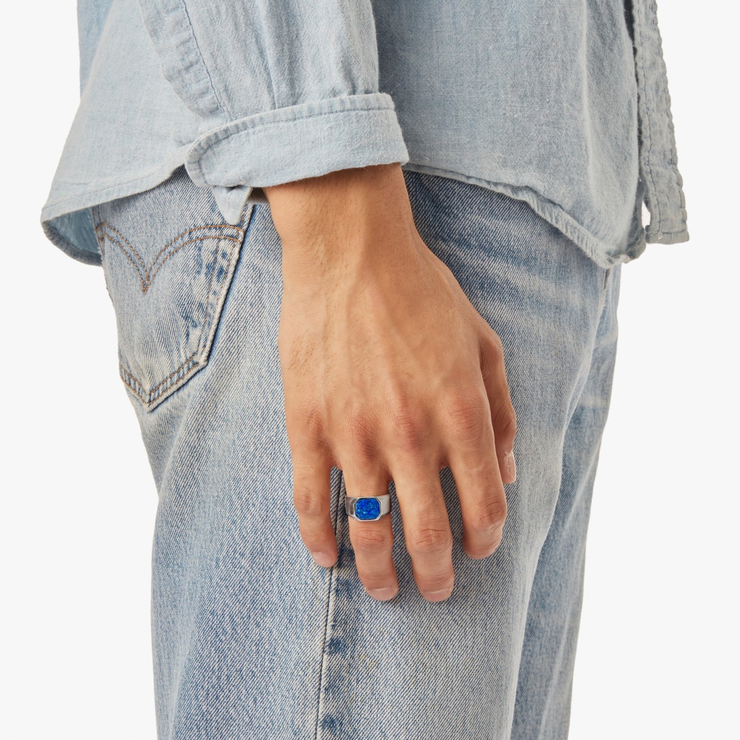 A person in a light blue denim shirt and jeans stands with their hand by their side, showcasing the Shinola Octagonal Lapis Signet Ring in sterling silver on their finger.