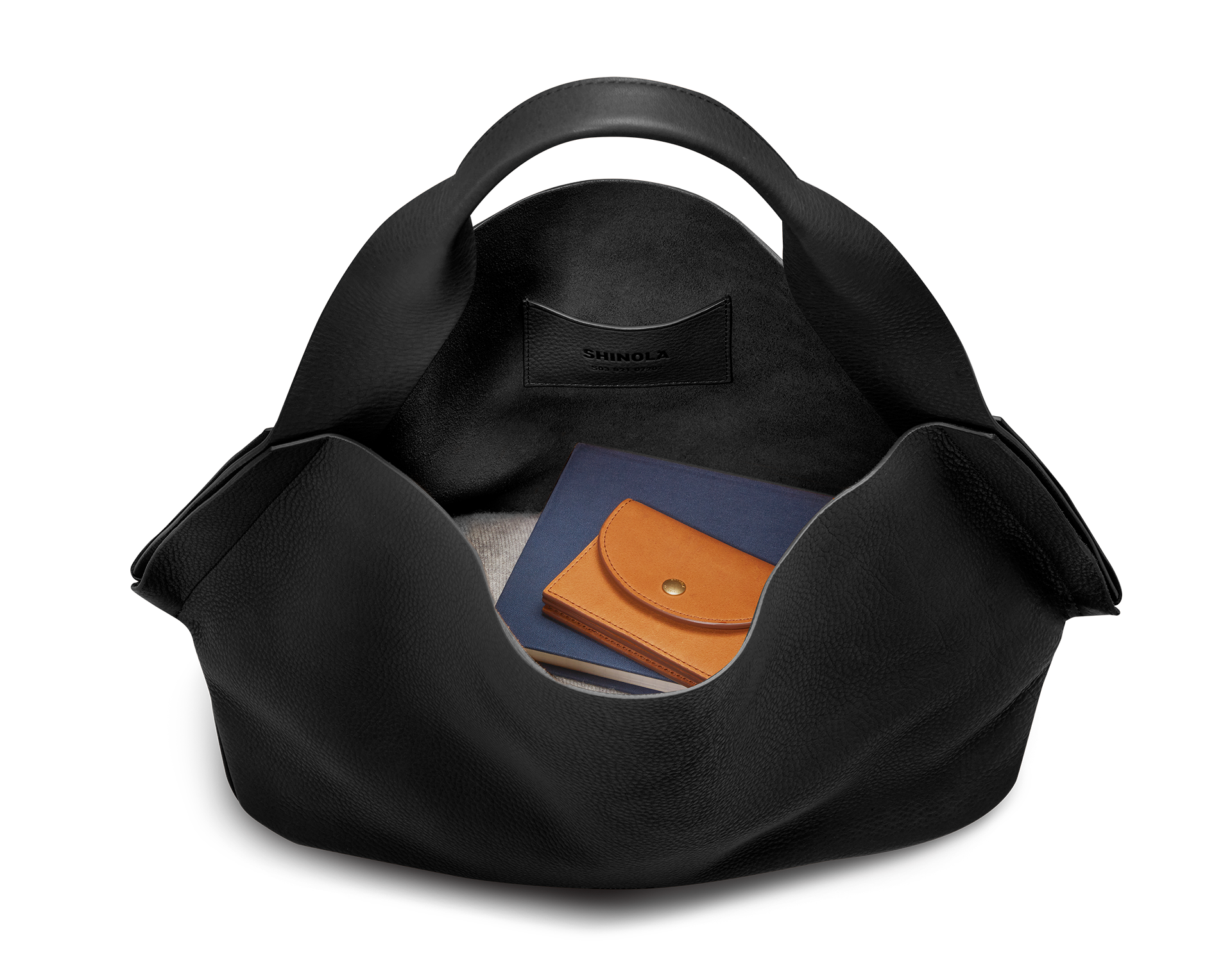 A black Derby Shoulder Bag by Shinola sits open on a plain white background, displaying a tan leather wallet and navy blue notebook inside its spacious interior with a leather card pocket stamped "Shinola.