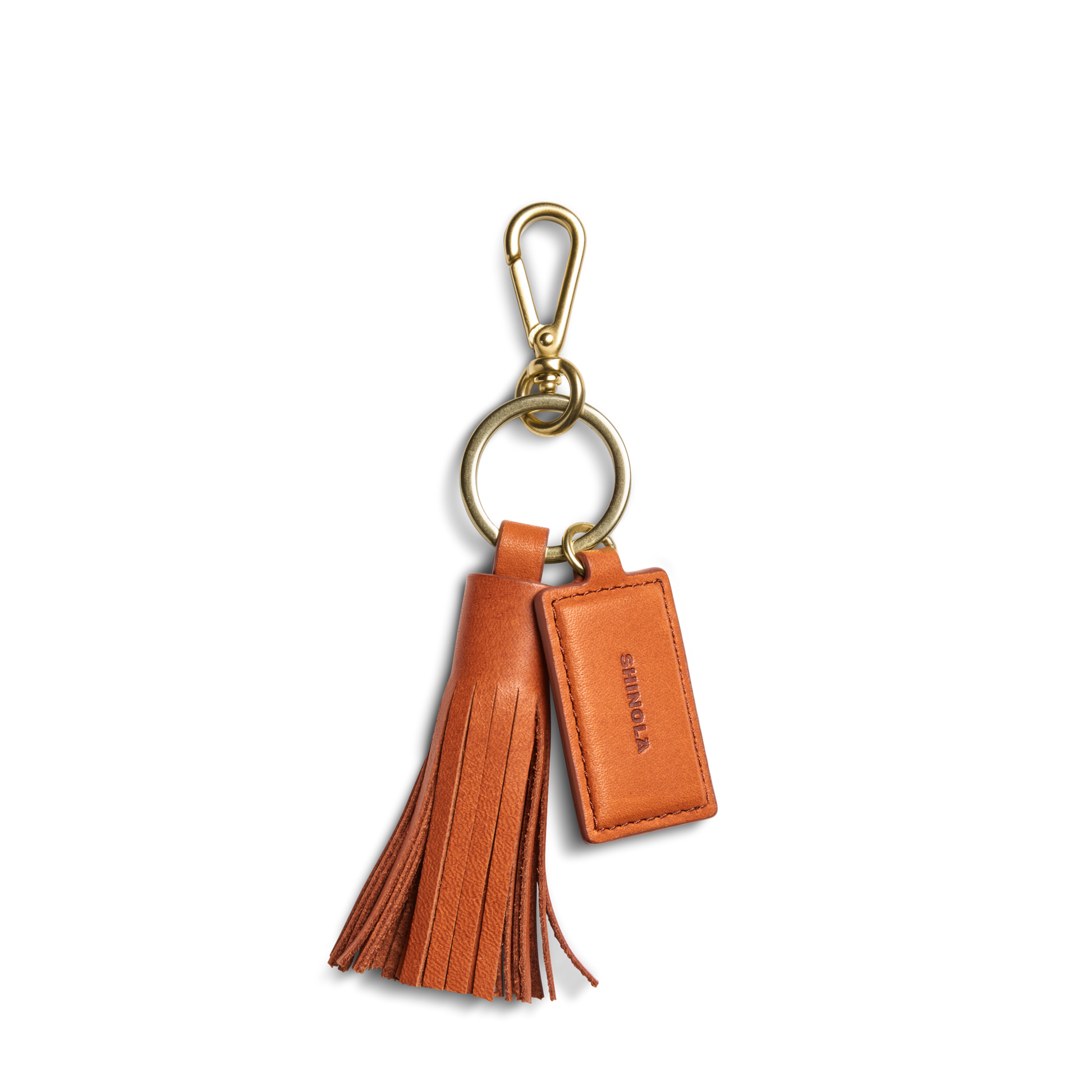 The Leather Tassel Keychain - Rust by Shinola features a gold clasp, large loop, and a rectangular embossed tag—monogrammable for a personalized touch.