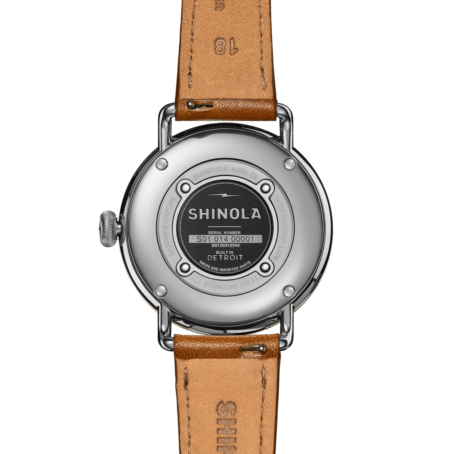 The back of a Shinola Canfield Watch with a round silver case, tan leather strap, and engraved details like the brand name, serial number, and "Built in Detroit" on the metal case back.