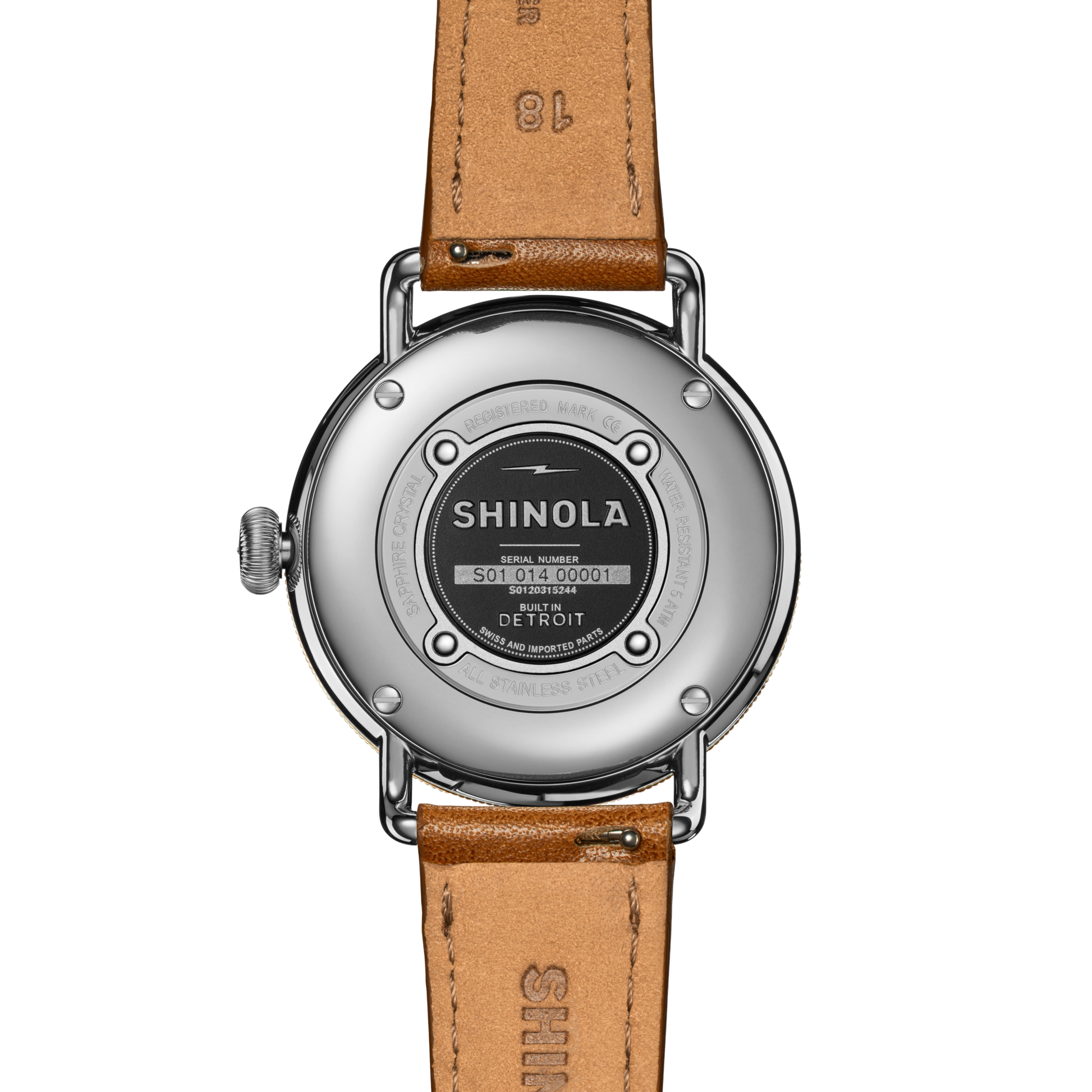 The back of a Shinola Canfield Watch with a round silver case, tan leather strap, and engraved details like the brand name, serial number, and "Built in Detroit" on the metal case back.