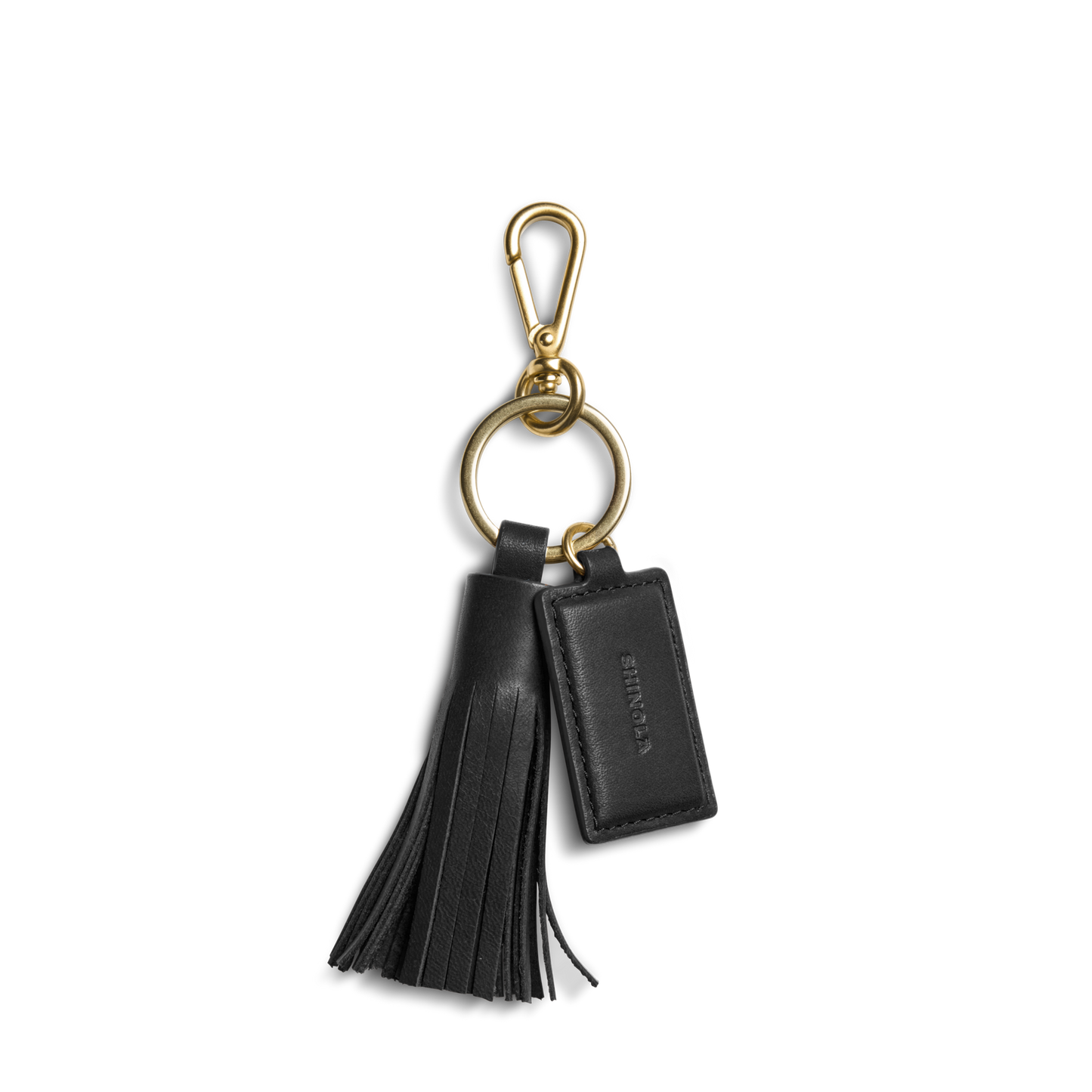 The Shinola Leather Tassel Keychain - Black features a gold clasp and ring, a black leather tassel, and a rectangular embossed tag—an elegant monogram keychain or stylish key fob.