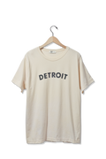 The Shinola Detroit Graphic T Shirt - Cream features bold black "DETROIT" lettering on the front and is displayed on a wooden hanger against a plain white background.