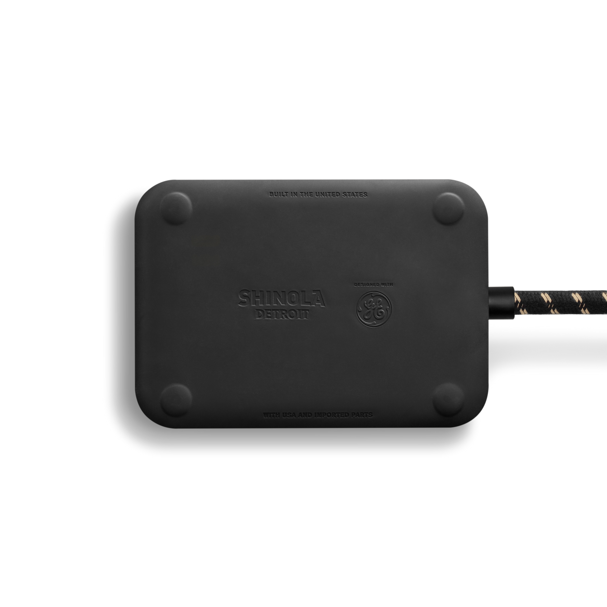A rectangular Shinola 5 Port Power Supply - Tangerine with rounded corners sits on a white background. A braided black and gold USB A+C cable is attached to its right side. The device features the Shinola logo and branding.