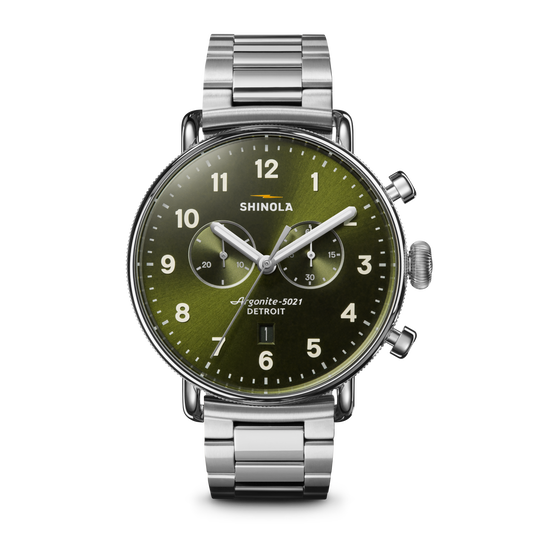The Shinola Canfield Chronograph Watch - Dark Olive features a silver case, dark olive dial with white numerals, three subdials, and a stainless steel link band, shown against a white background.