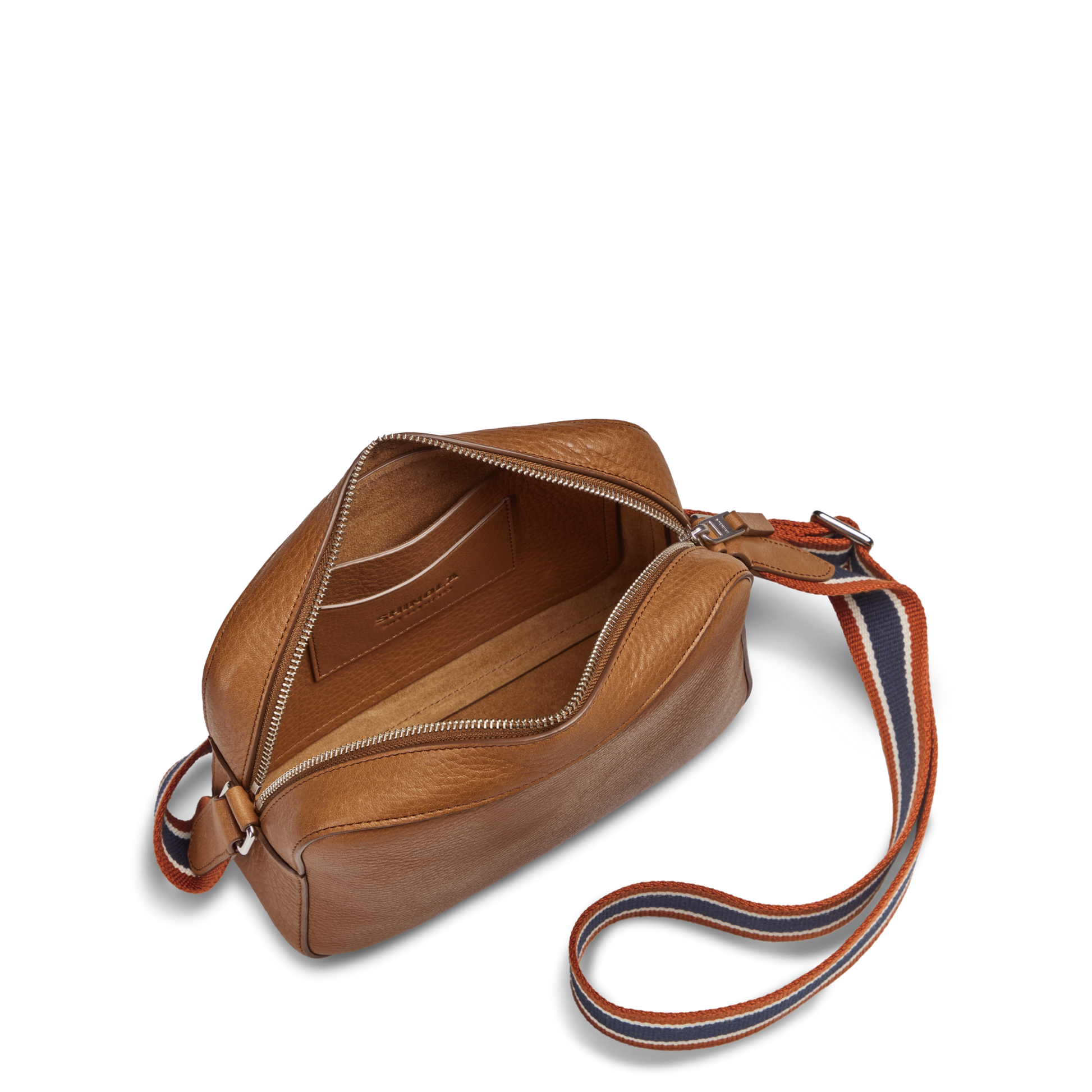 The Shinola Camera Crossbody Bag - Tan, featuring a striped adjustable strap, is shown open on a white background to reveal its spacious interior and inner pocket.