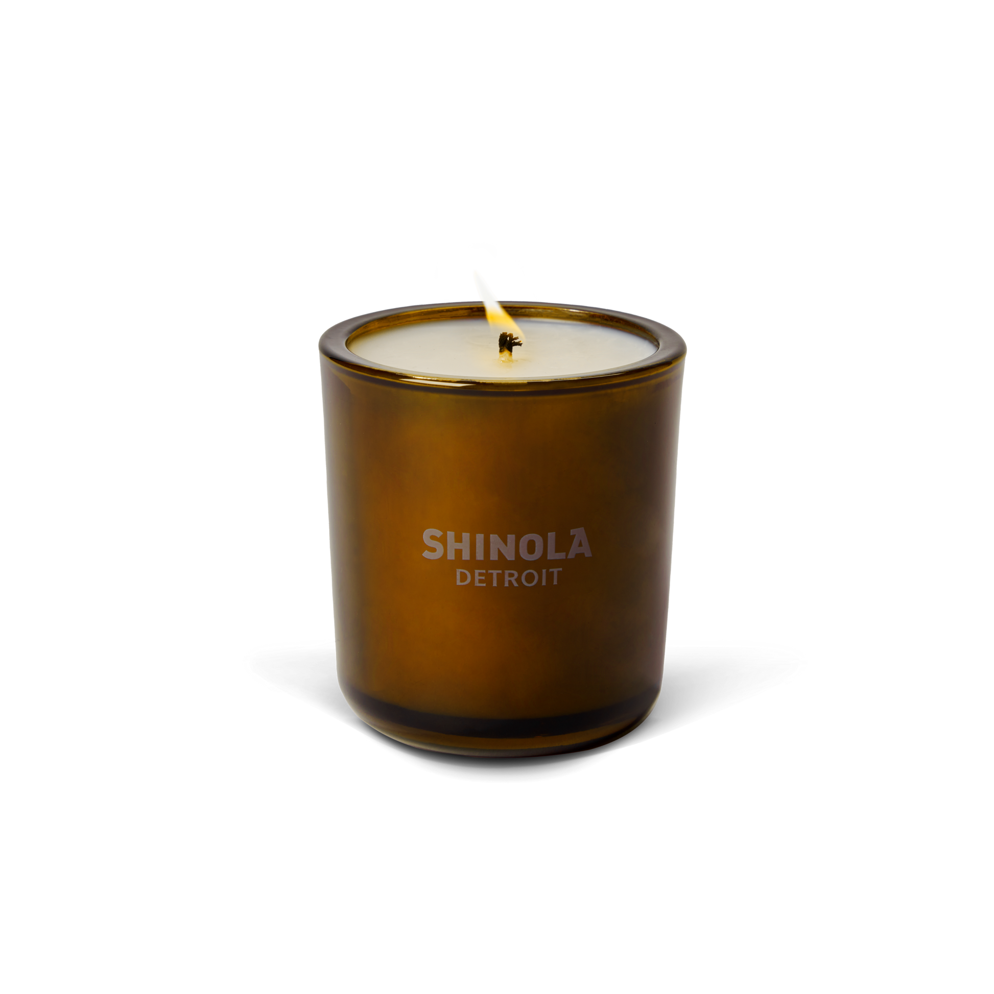 The Shinola Smoke 8oz Scented Candle, shown with a lit wick in brown glass against a white background, features "Shinola Detroit" on the front and is crafted from coconut soy wax for a clean, lasting burn.
