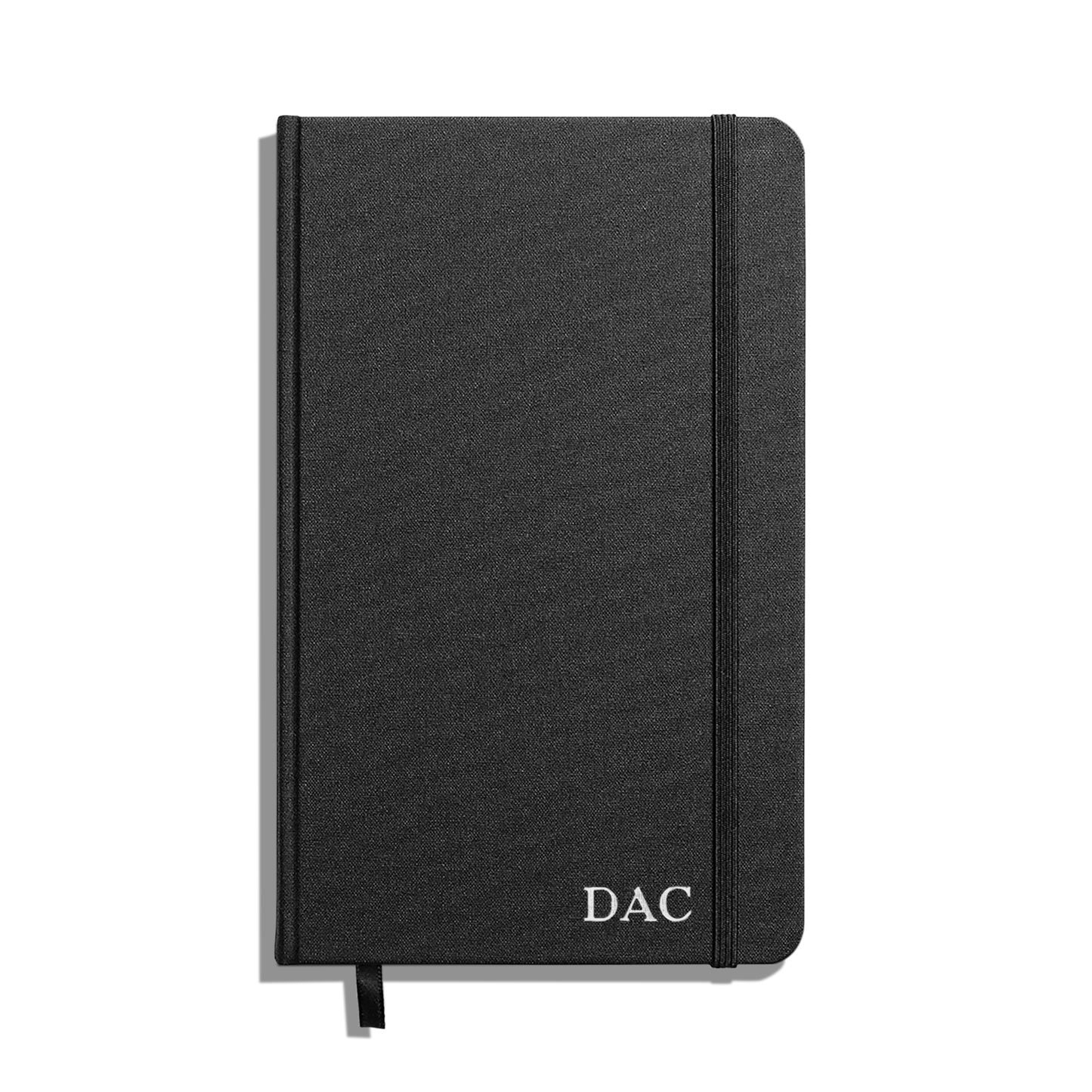 The Shinola Medium Hard Grid Journal in black features a hardcover, smyth-sewn binding, elastic band closure, and white DAC initials on the bottom right corner of the cover.