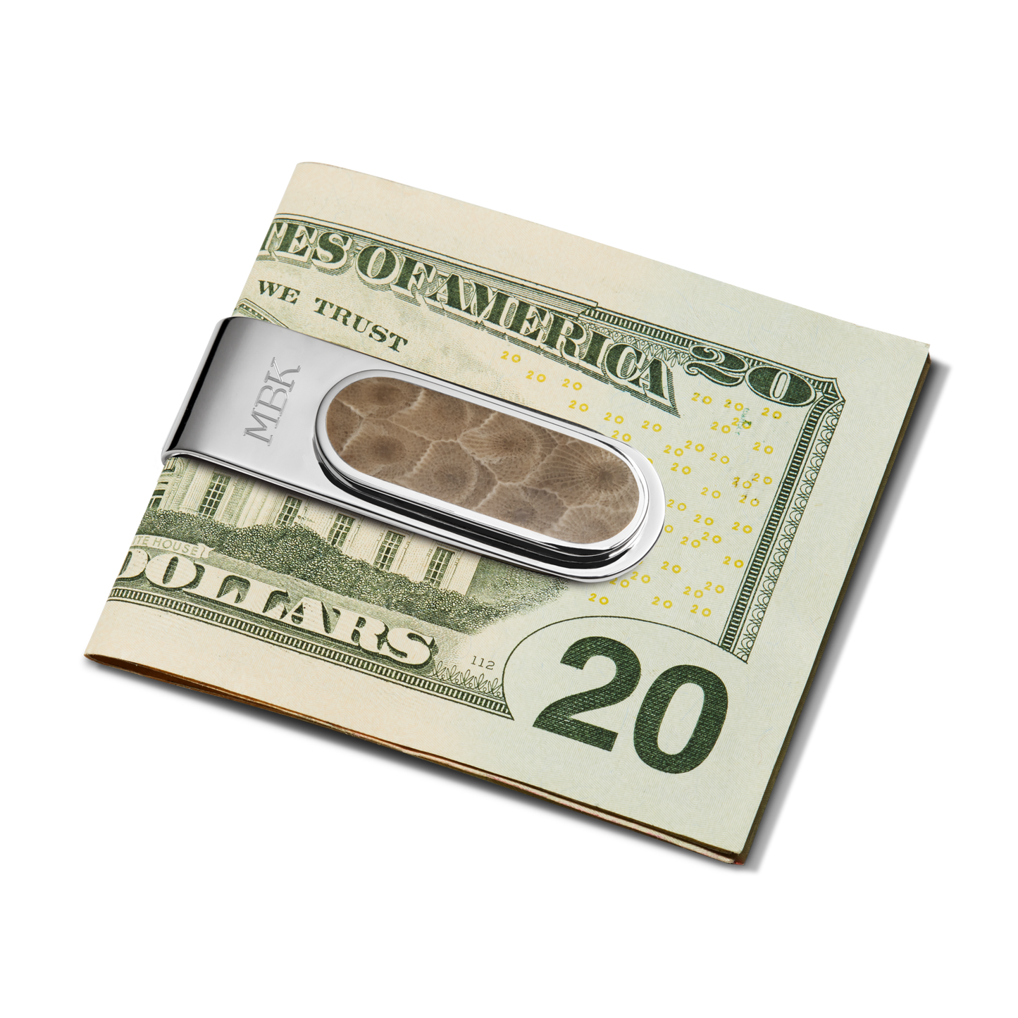 A folded twenty-dollar bill is held by the Shinola Petoskey Money Clip—sterling silver with a brown textured center resembling Petoskey stone and "MBK" engraved on the side—on a white background.