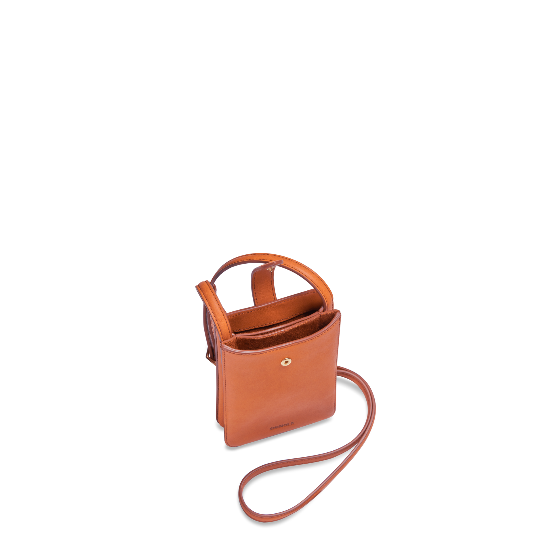 The Shinola Bixby Phone Crossbody in Rust is a small, rectangular natural leather bag with two handles, a long shoulder strap, and a snap button closure, shown against a white background.