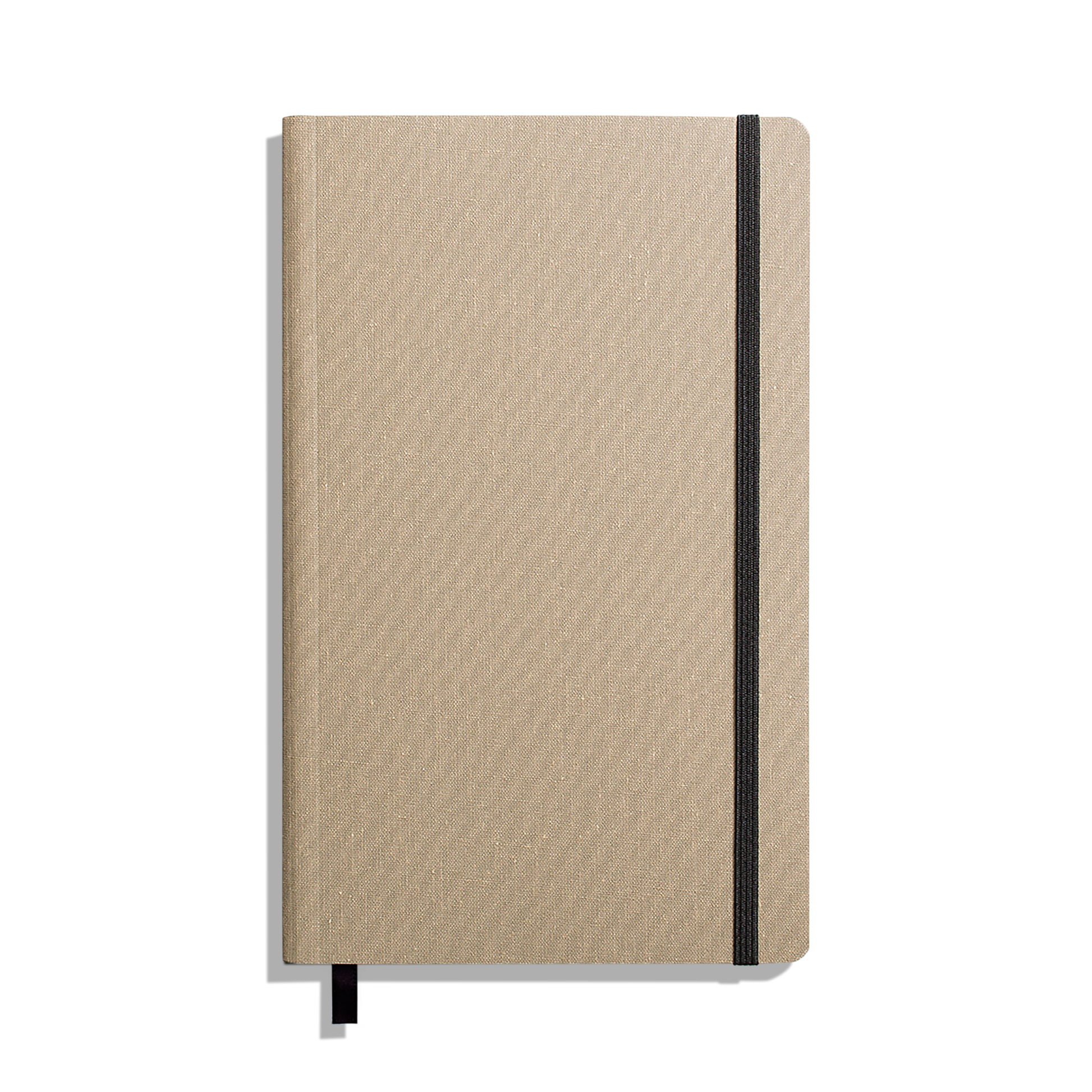 The Shinola Medium Soft Ruled Journal - Oat is shown closed with a textured beige cover, black elastic band on the right, and a black ribbon bookmark against a white background. Features durable smyth-sewn binding.