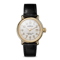 The Shinola Runwell Watch - Alabaster features a gold stainless steel case, white dial with black numerals, gold hands, date display, and a black leather strap, displayed on a plain white background.