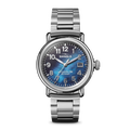 The Shinola Runwell Watch - Cadet Blue features a stainless-steel case and bracelet, cadet blue mother of pearl dial, white numerals, and a date window at 3 o’clock, shown against a plain white background.