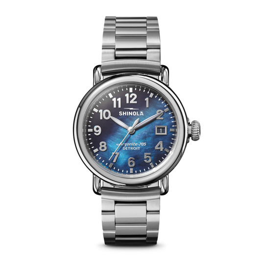 The Shinola Runwell Watch - Cadet Blue features a stainless-steel case and bracelet, cadet blue mother of pearl dial, white numerals, and a date window at 3 o’clock, shown against a plain white background.