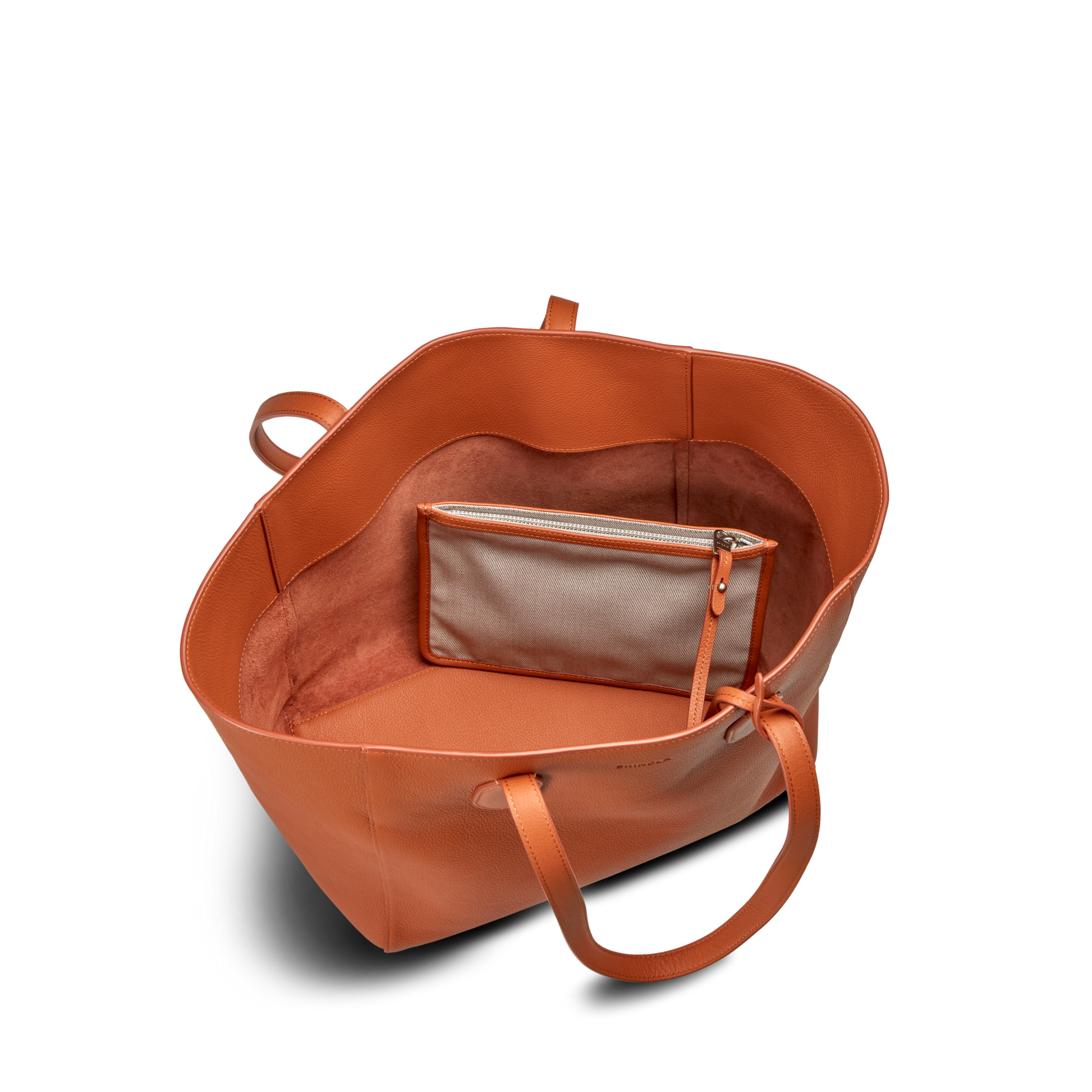 The Shinola Runabout Tote Bag - Rust features a large orange pebbled leather design with two handles, an open spacious interior, and an attached small beige zipper pouch inside.