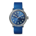 The Shinola Detrola Watch - Denim Blue features a round face with white numerals, silver hands, a date window at 3 o’clock, and a matching blue leather strap. The watch reads 1:11.