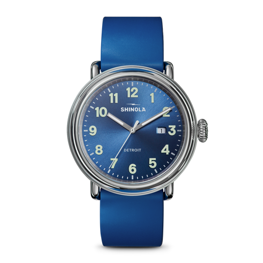 The Shinola Detrola Watch - Denim Blue features a round face with white numerals, silver hands, a date window at 3 o’clock, and a matching blue leather strap. The watch reads 1:11.
