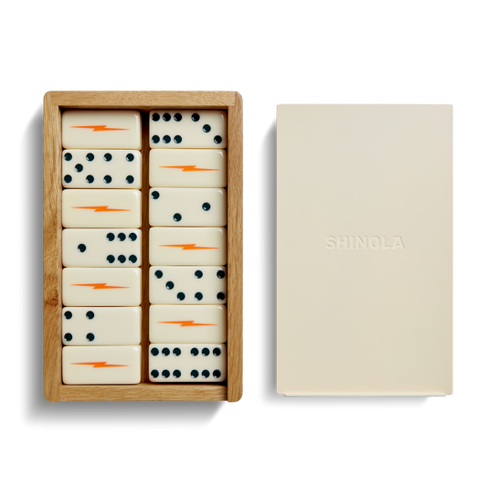 The Dominoes Set - Cream / Blue by Shinola features hand-painted tiles with blue dots and orange lightning bolts, housed in a wooden box next to a closed beige box embossed with the SHINOLA logo.