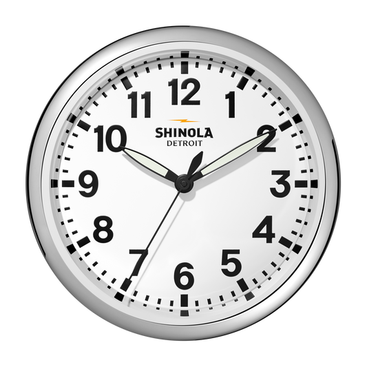 The 14" Runwell Clock by Shinola features a white face, chrome casing, black numbers, and black hour and minute hands set to 1:50:34. The Shinola brand name is displayed on this classic wall clock.