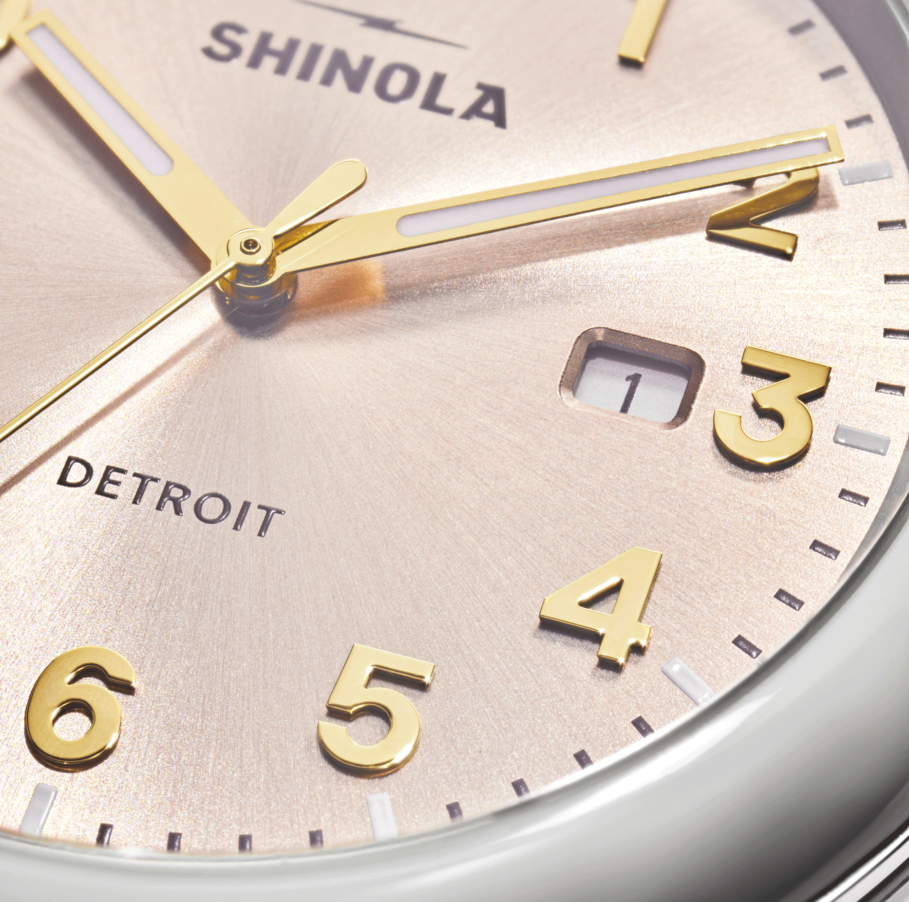 Close-up of the Shinola Detrola Watch - Nude featuring classic American design with gold hands and numbers, a light metallic background, and a date window showing the number 1 between the 3 and 4 markers.
