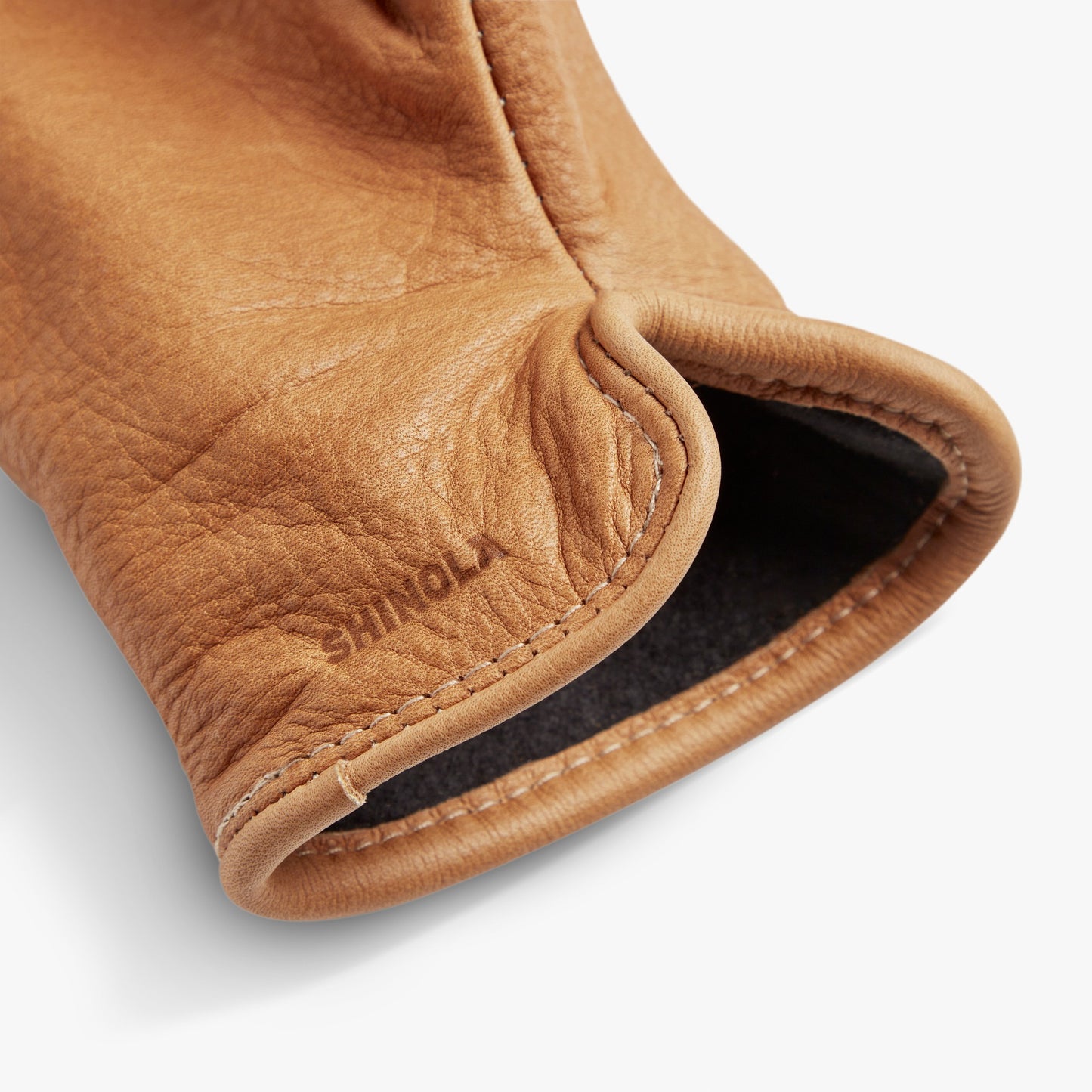 Close-up of the cuff of a black bovine leather glove with visible stitching and the Shinola brand name embossed near the edge. The inner lining is a soft, dark fleece, highlighting these quality gloves sewn in the USA.