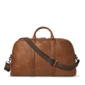The Shinola Runwell Duffle Bag in Medium Brown is crafted from premium leather, with sturdy handles and an adjustable, detachable shoulder strap. Displayed on a white background, it's an ideal spacious carry-on for any journey.