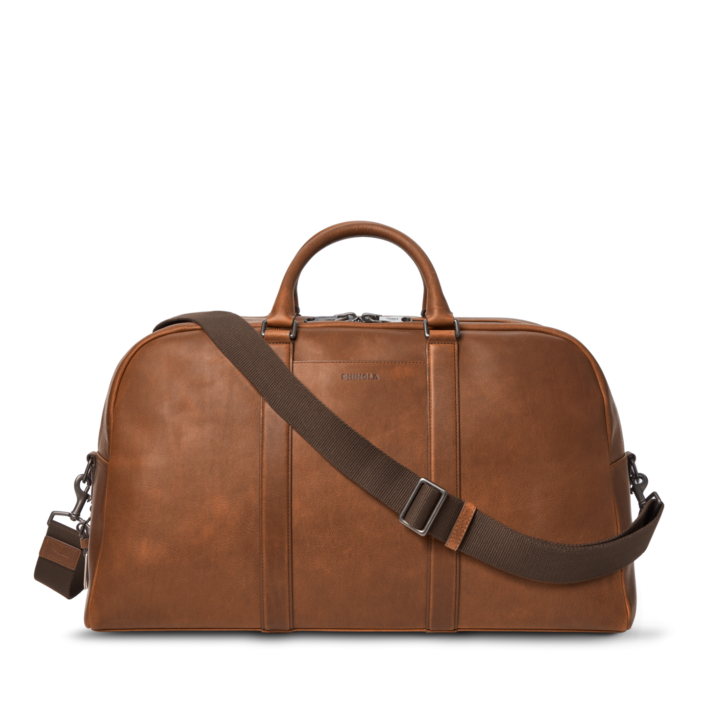 The Shinola Runwell Duffle Bag in Medium Brown is crafted from premium leather, with sturdy handles and an adjustable, detachable shoulder strap. Displayed on a white background, it's an ideal spacious carry-on for any journey.