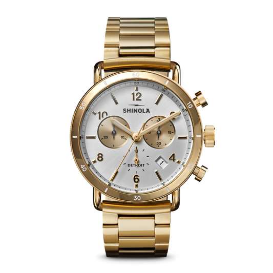 The Shinola Canfield Sport Chronograph Watch - Silver features a gold stainless steel case, silver dial with two subdials, date display, gold hour markers, three side buttons, and a matching gold metal bracelet.