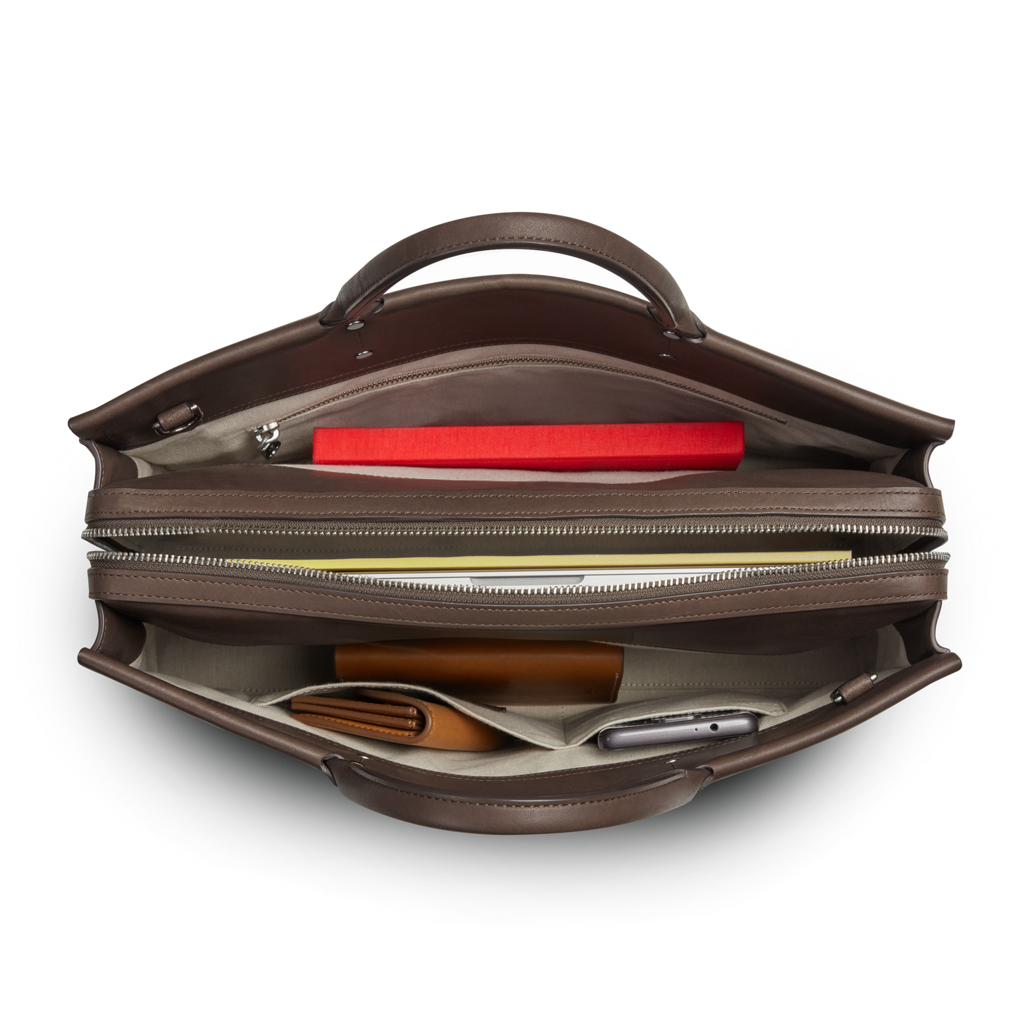 Top view of the Shinola Day Satchel - Espresso with a red notebook, pen, brown wallet, and smartphone neatly organized in separate compartments—ideal for keeping your essentials ready while on the go.