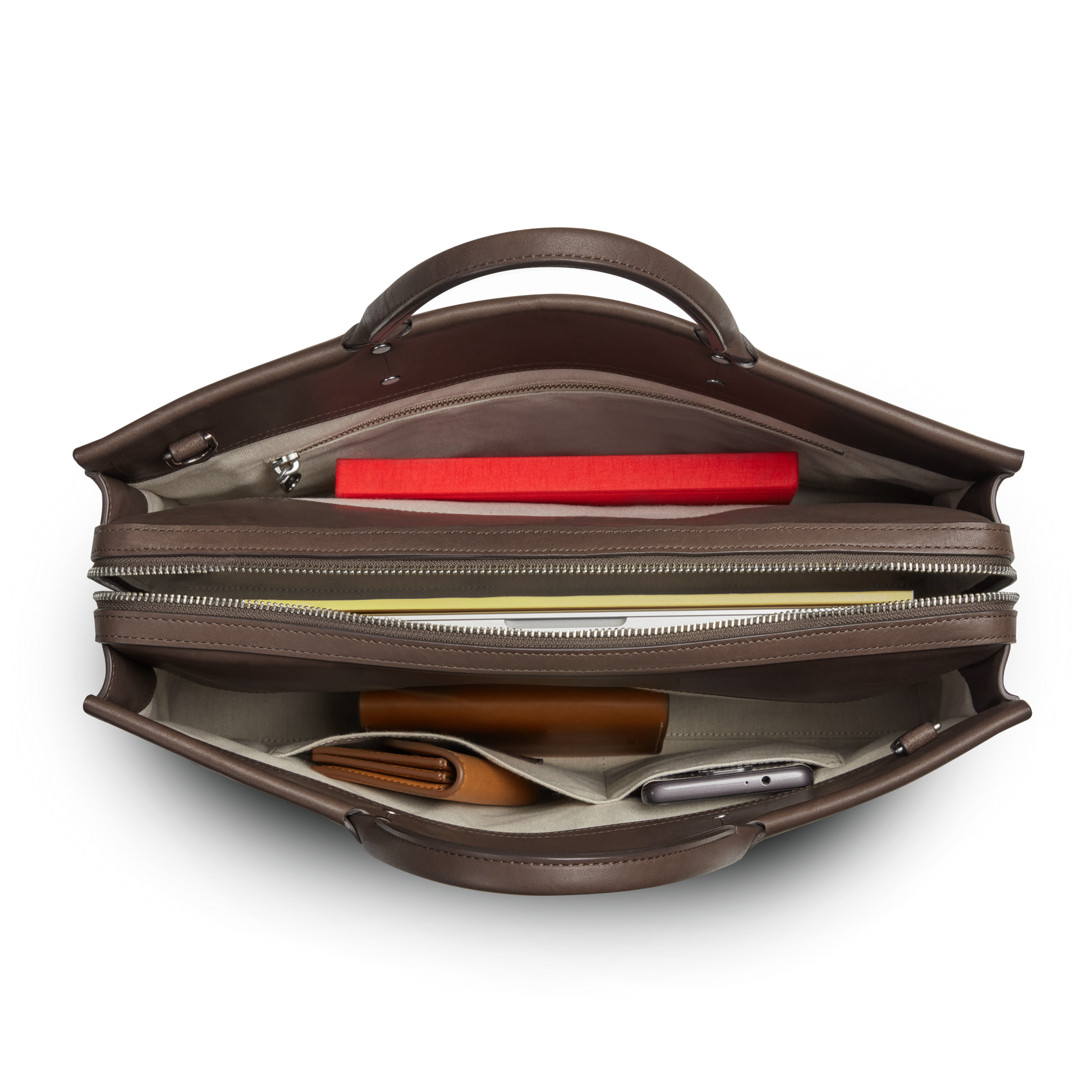 Top view of the Shinola Day Satchel - Espresso with a red notebook, pen, brown wallet, and smartphone neatly organized in separate compartments—ideal for keeping your essentials ready while on the go.