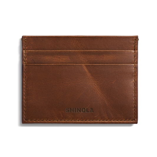 The Shinola 5 Pocket Card Holder in medium brown leather offers RFID protection, two card slots, visible edge stitching, and “SHINOLA” embossed at the bottom center, shown on a plain white background.