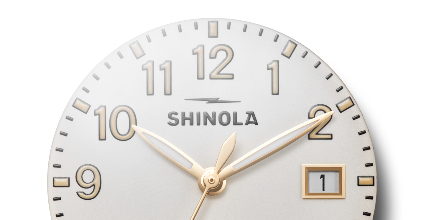 Close-up of the Shinola Runwell Watch - Alabaster, featuring a gold stainless steel case with gold hour, minute, and second hands set at 10:10:08. The date window shows "1" on a white background with bold black numerals.