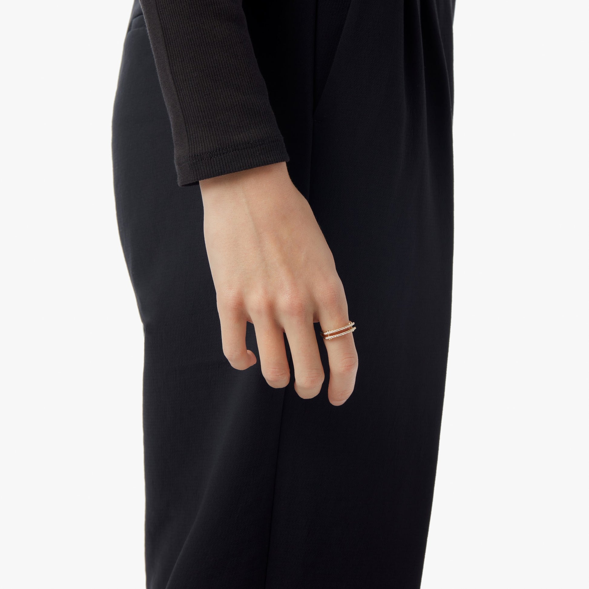 A person in a black long-sleeve outfit, shown shoulder to knee, displays the Shinola Diamond Pave Rivet Double Row Ring in yellow gold on their index finger.