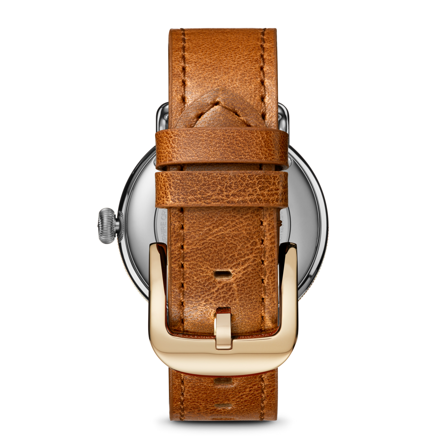 A close-up of the Shinola Canfield Watch shows its silver case and tan leather strap with visible stitching and a gold buckle.