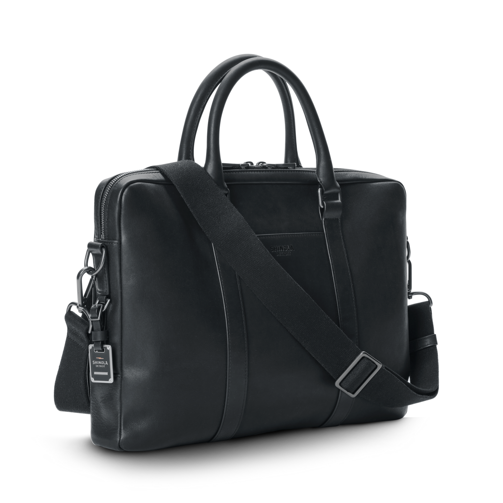 The shinola.momputer Briefcase in black features two handles, a removable adjustable shoulder strap, and a small luggage tag, shown against a plain white background.