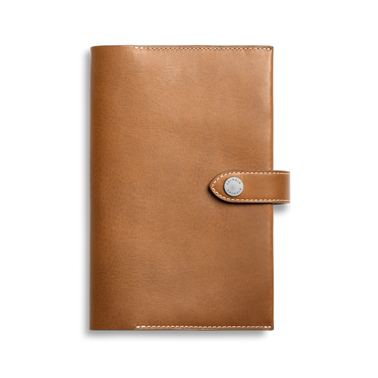 The Shinola Medium Snap Journal Cover in Tan Vachetta features visible edge stitching and a snap-button closure, crafted from Italian leather, shown against a plain white background.