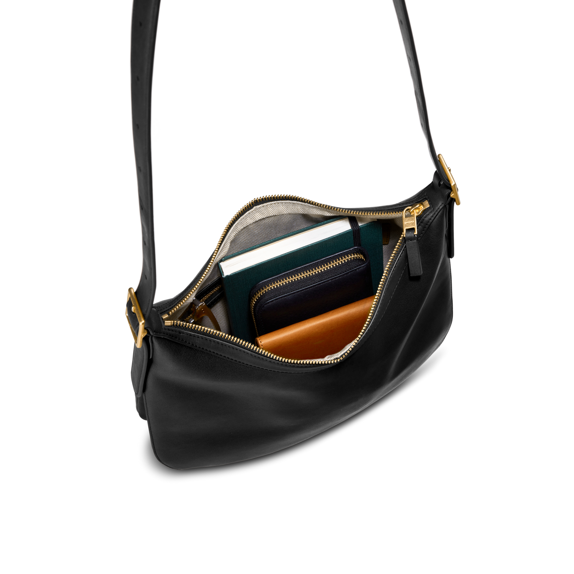 The Medium Bixby Crossbody - Black by Shinola, crafted from black leather with a gold zipper, is shown open to display a navy blue wallet, brown wallet, and green notebook arranged inside—all set against a white background.