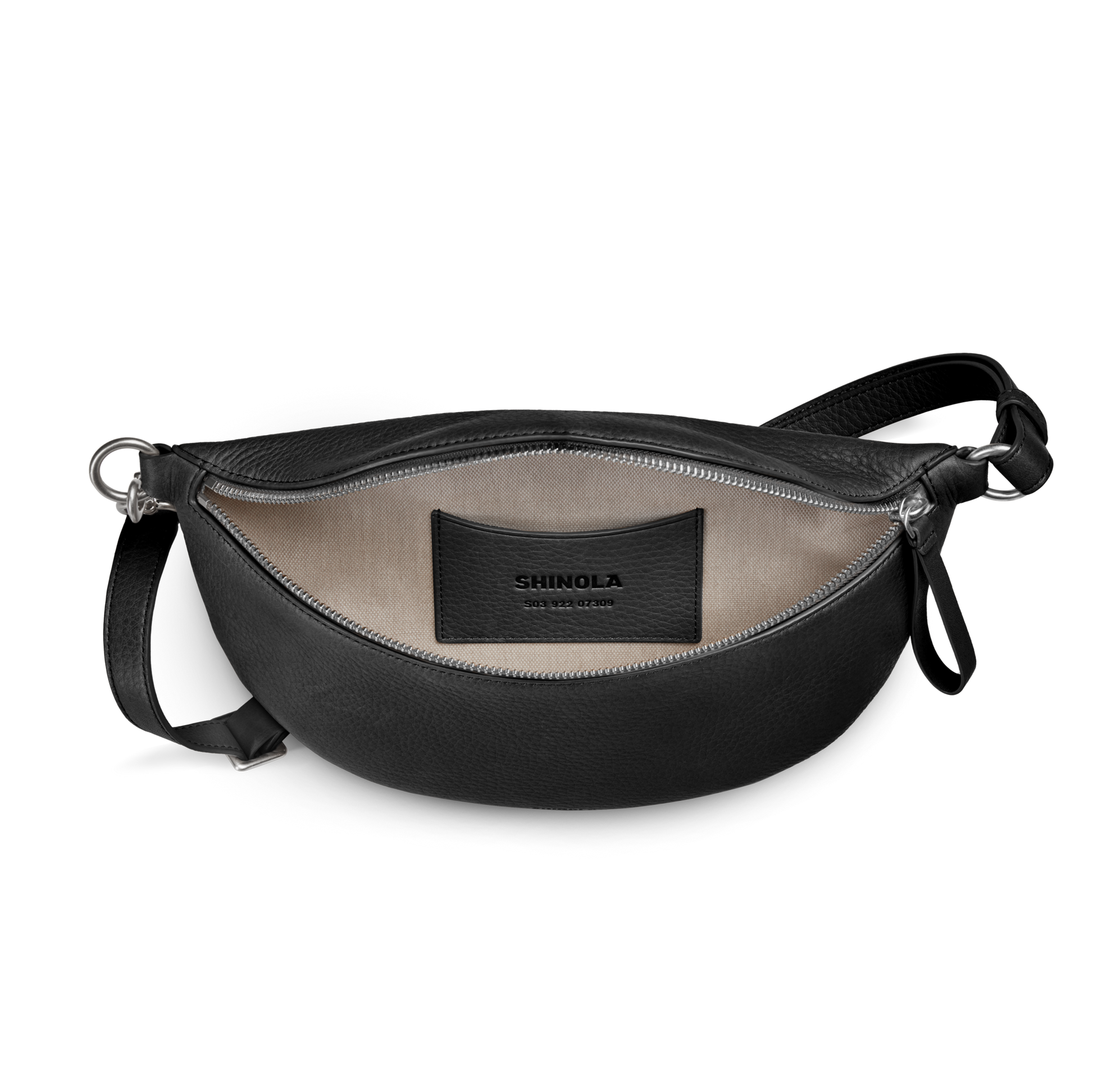 The Shinola Sling Bag - Black is a leather crossbody with a beige interior, small inside pocket, black Shinola patch, adjustable strap, and unzipped for easy access.