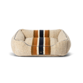 The Shinola Kuddle Dog Bed - Stripe Oat is a rectangular, plush beige bed with orange, navy blue, and brown stripes, raised sides, soft textured surface, memory fiber fill, minimalist design, and a washable cover.