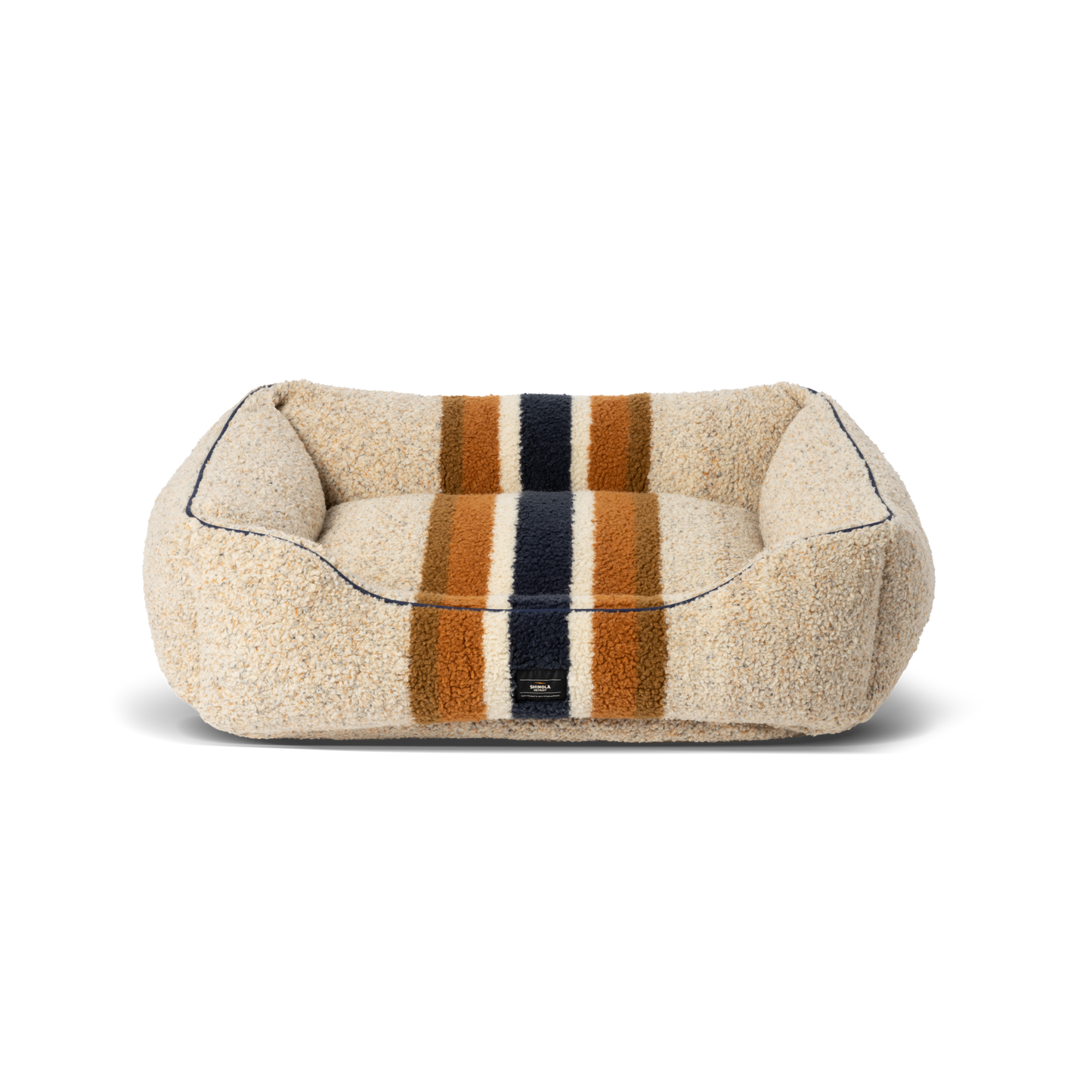 The Shinola Kuddle Dog Bed - Stripe Oat is a rectangular, plush beige bed with orange, navy blue, and brown stripes, raised sides, soft textured surface, memory fiber fill, minimalist design, and a washable cover.