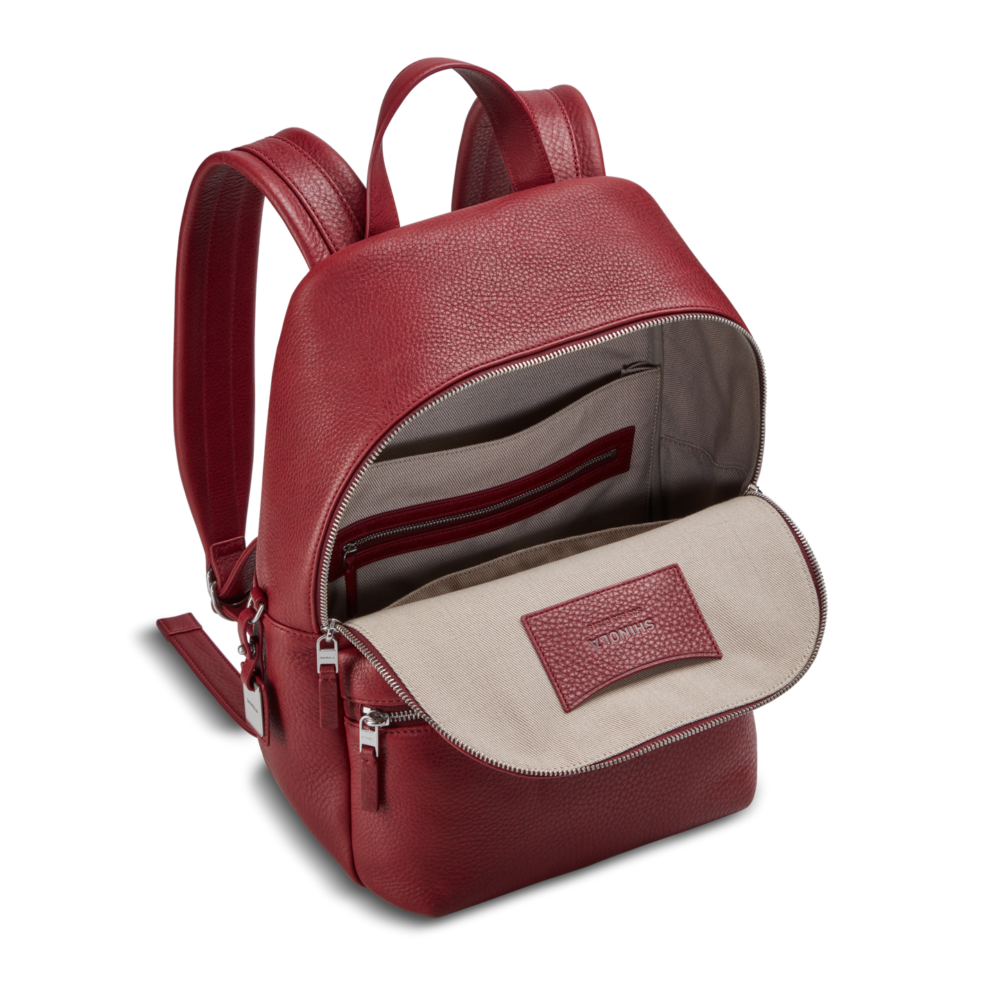 The Shinola Small Runwell Backpack - Ruby features red Natural Grain Leather, a beige fabric lining, open main compartment, inside zip pocket, padded straps, silver zippers, and an interior label.