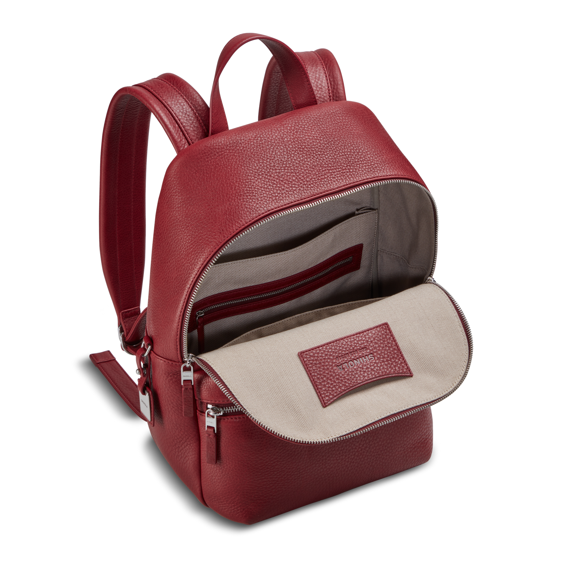 The Shinola Small Runwell Backpack - Ruby features red Natural Grain Leather, a beige fabric lining, open main compartment, inside zip pocket, padded straps, silver zippers, and an interior label.