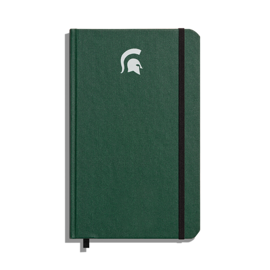 The Shinola Medium Hard Ruled Journal - Forest features a green hardcover, elastic band closure, white Spartan helmet logo on the front, and acid-free paper—perfect for lasting Michigan State University notes.