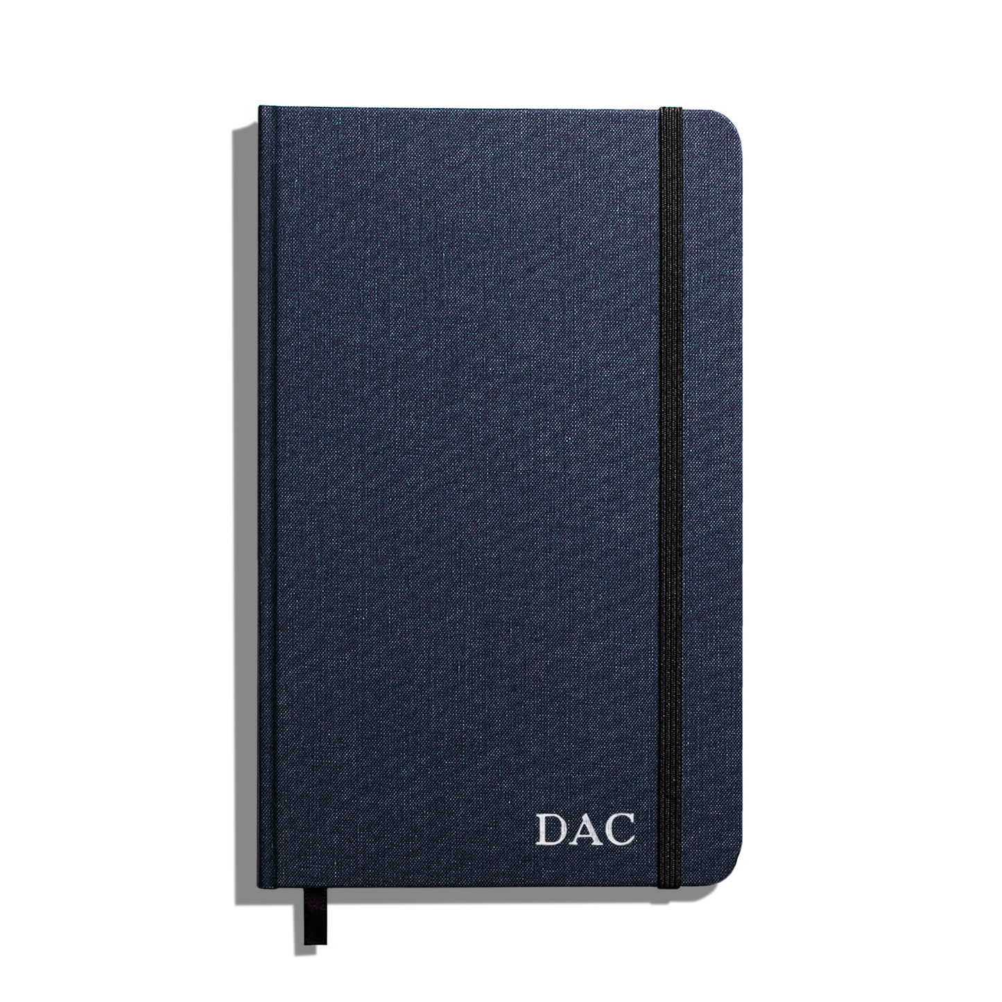 The Shinola Medium Hard Grid Journal in navy features a durable linen cover, black elastic band, and ribbon bookmark, with "DAC" initials in white. Crafted with smyth-sewn binding and acid-free paper for lasting quality.