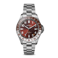 The Shinola Monster GMT Automatic Watch - Whiskey features a stainless steel case, metallic red-brown dial, silver and white hour markers, date at 3 o’clock, 24-hour GMT bezel, and a silver link bracelet.