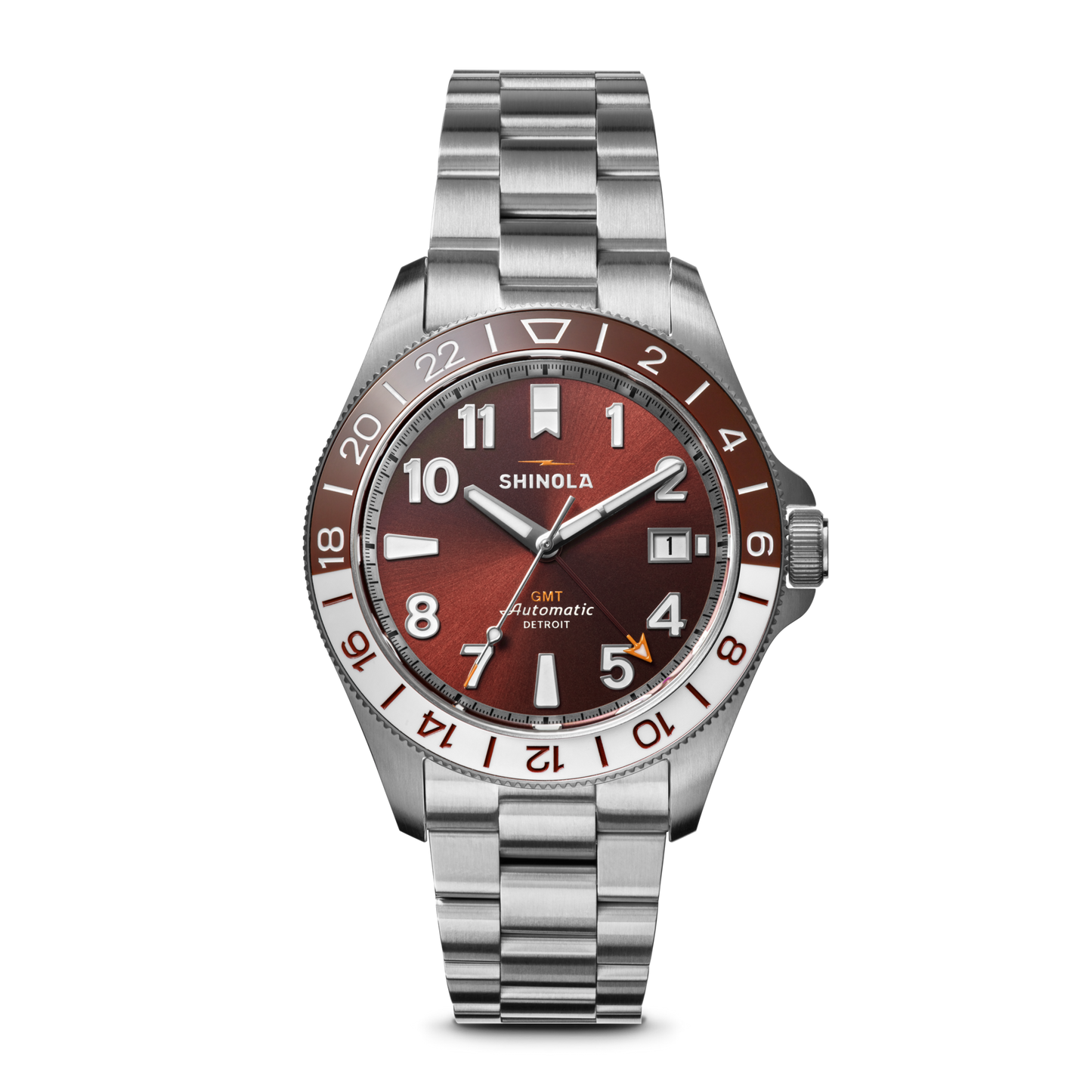 The Shinola Monster GMT Automatic Watch - Whiskey features a stainless steel case, metallic red-brown dial, silver and white hour markers, date at 3 o’clock, 24-hour GMT bezel, and a silver link bracelet.
