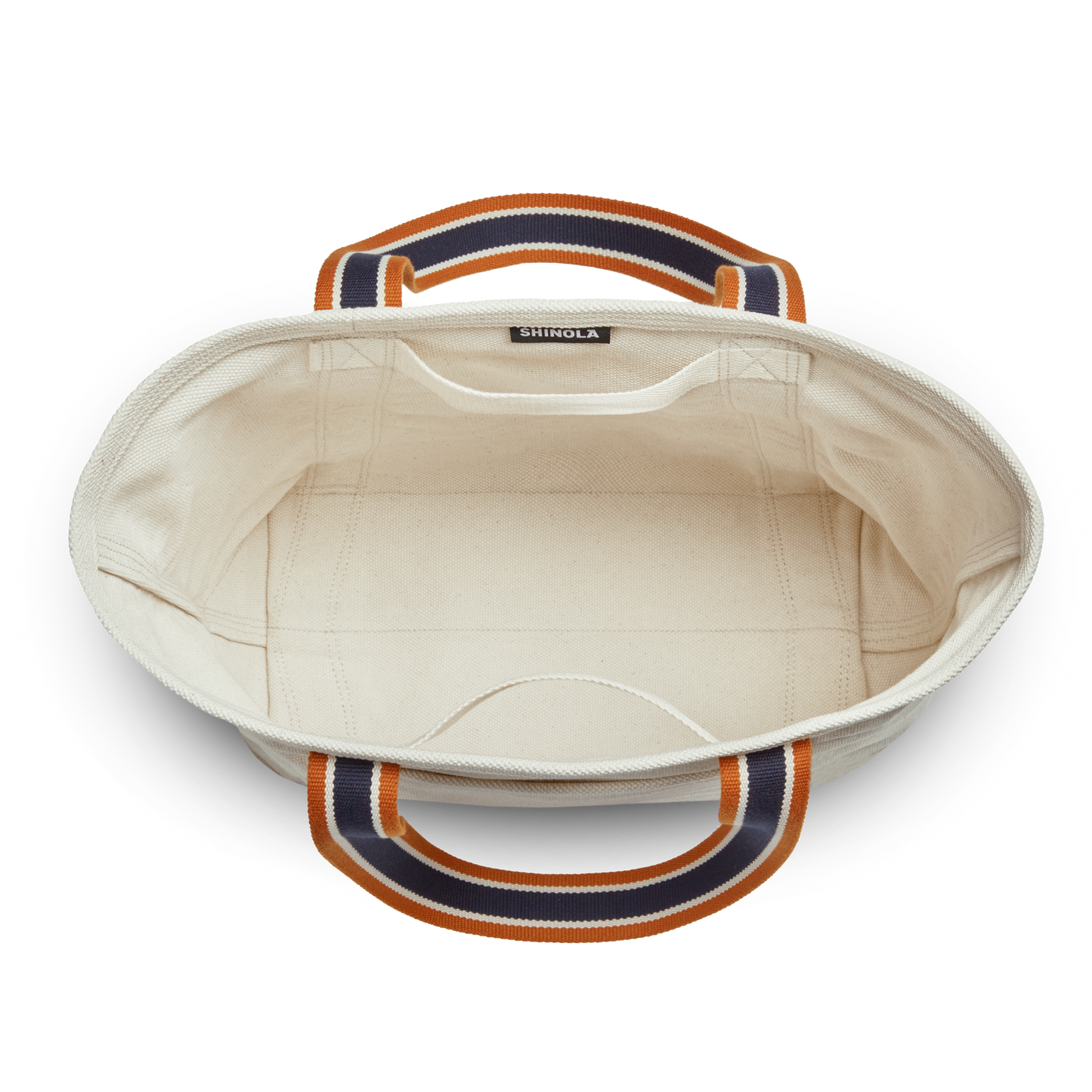 Top view of the Shinola Small Easy Canvas Tote - Natural, a cream tote with navy blue and orange striped handles. Ideal for daily essentials, it features a plain interior, visible stitching, and an inner seam label.